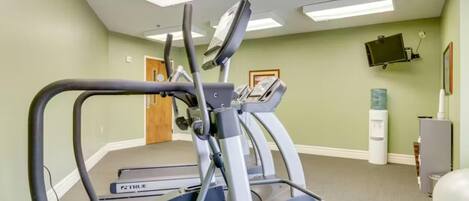 A fitness room with treadmills, a water dispenser, and a TV mounted on the wall.