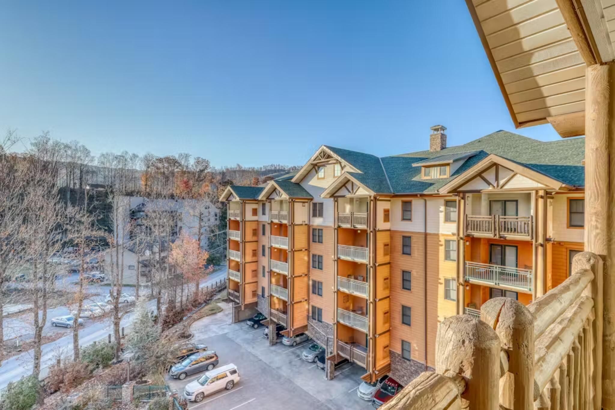 A multi-story hotel with balconies, a parking lot, and a view of trees and a clear sky.