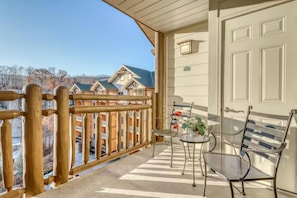 A balcony with a wooden railing, a door, and two chairs with a small table and a potted plant. - Baskins Creek 512 (Gatlinburg)