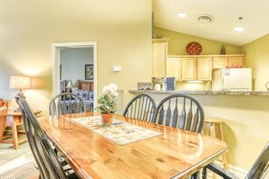 A dining area with a wooden table, chairs, a potted plant, and a kitchen in the background. - Baskins Creek 512 (Gatlinburg)