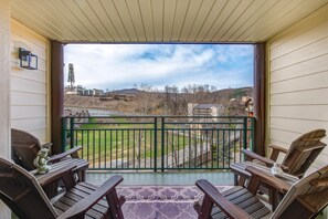 Ein Balkon mit Holzkufen und einem gemusterten Teppich, der auf eine Grünfläche und Gebäude in der Ferne blickt.