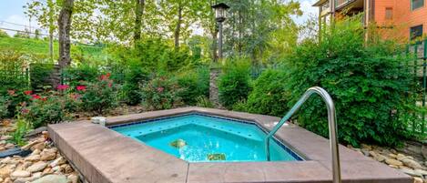 A rectangular hot tub surrounded by a stone border, with a metal ladder leading into it.