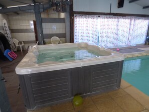 Un jacuzzi en una habitación con paredes de azulejos, una ventana con cortinas y una piscina en el exterior.
