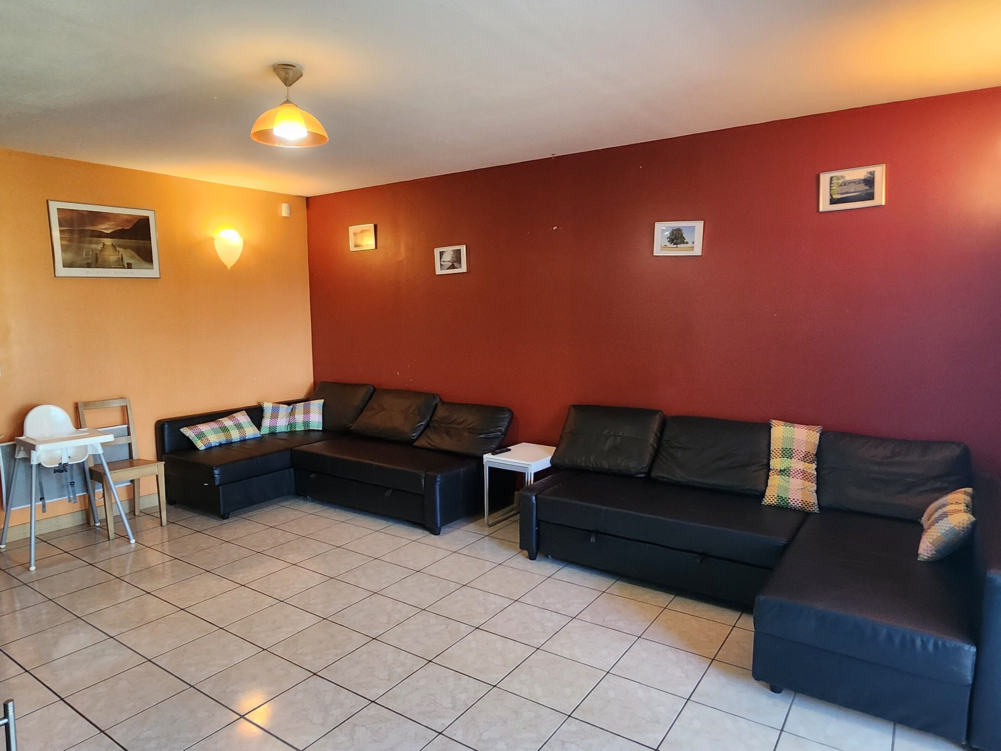 A living room with a sofa, a small table, a high chair, and a ceiling light.