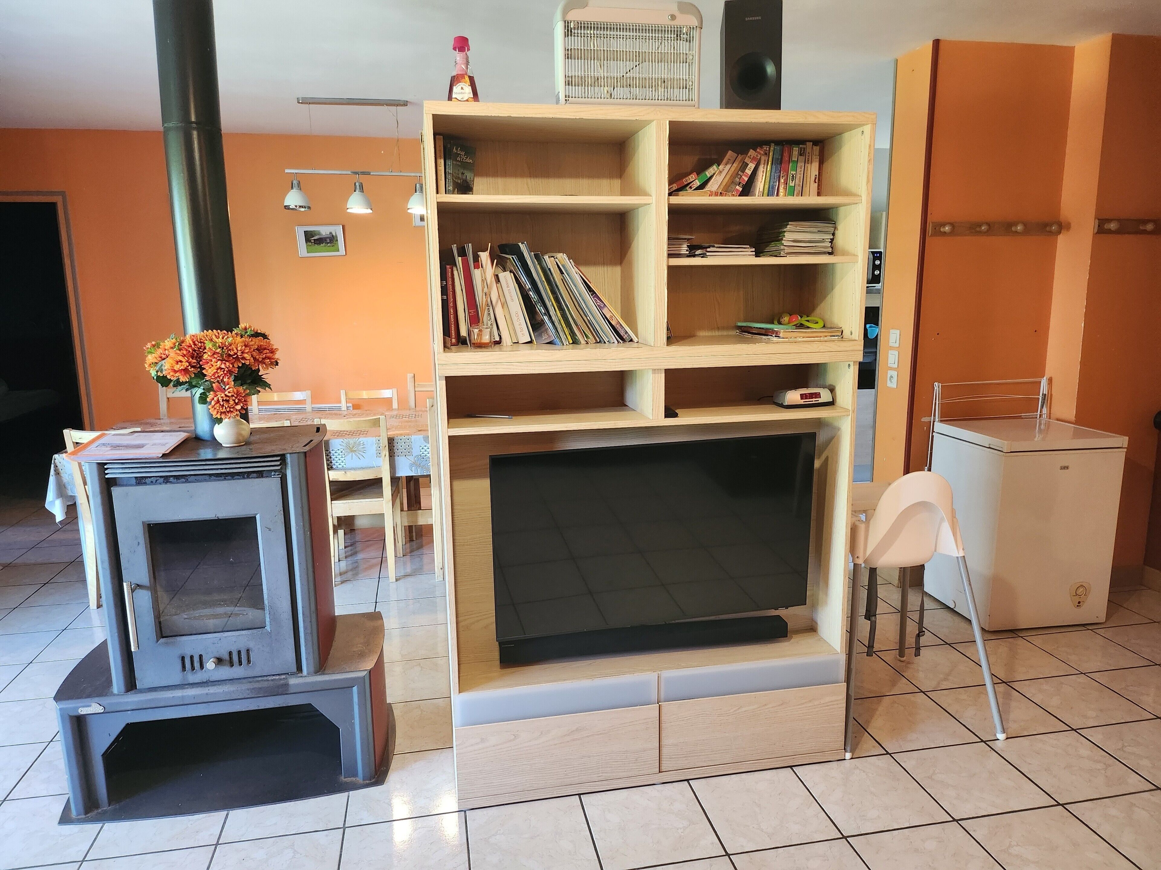 Un salon avec une cheminée, une bibliothèque, une table à manger avec des chaises et un radiateur blanc.