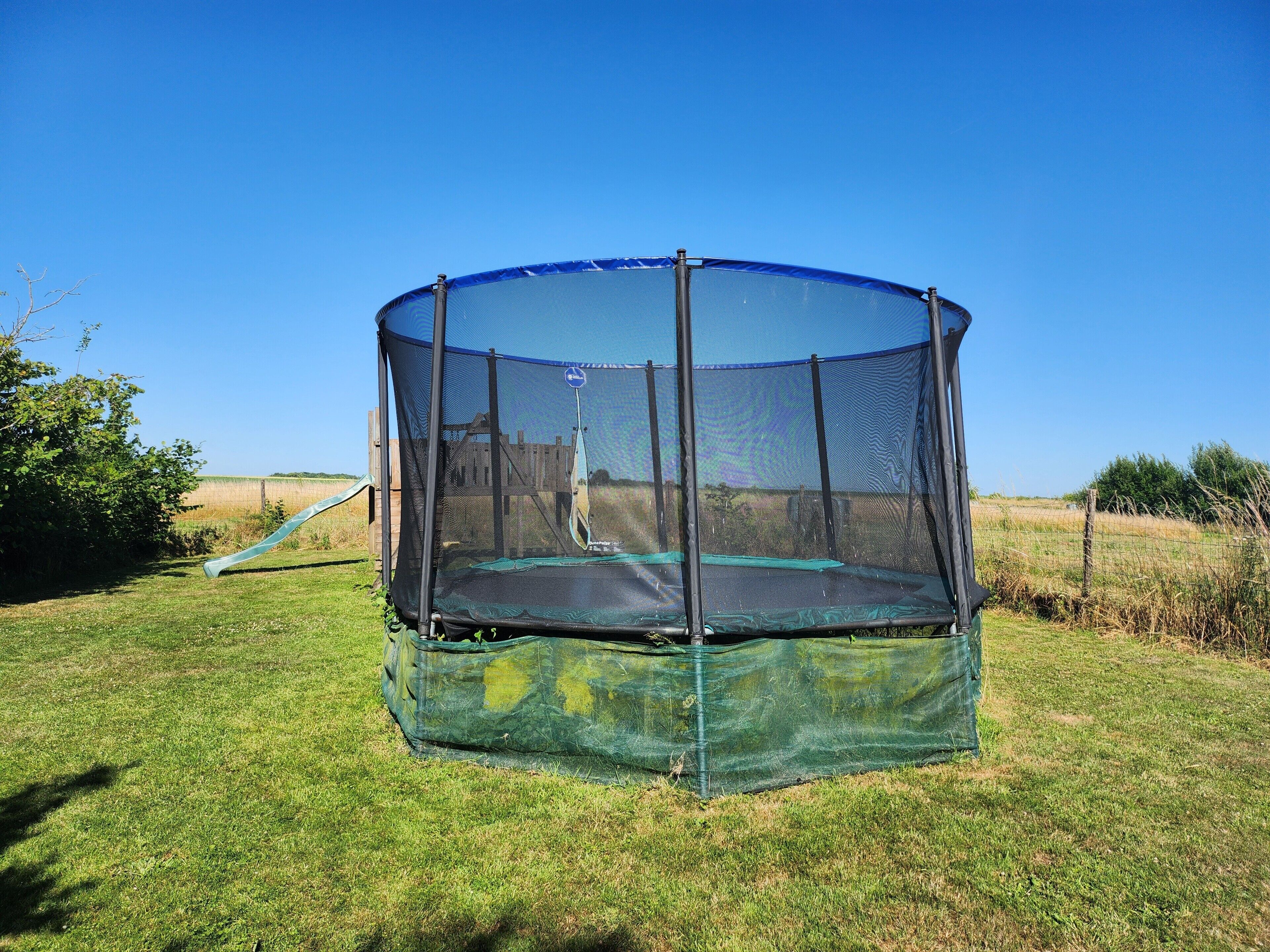 Ein runder Trampolin mit Sicherheitsnetz in einer grünen Wiese.