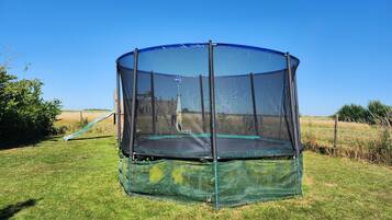 Ein runder Trampolin mit Sicherheitsnetz in einer grünen Wiese.