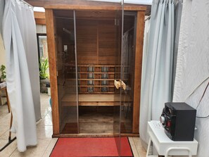A room with a sliding glass door leading to a wooden interior, a red mat at the entrance, and a black electronic device on a white stand.