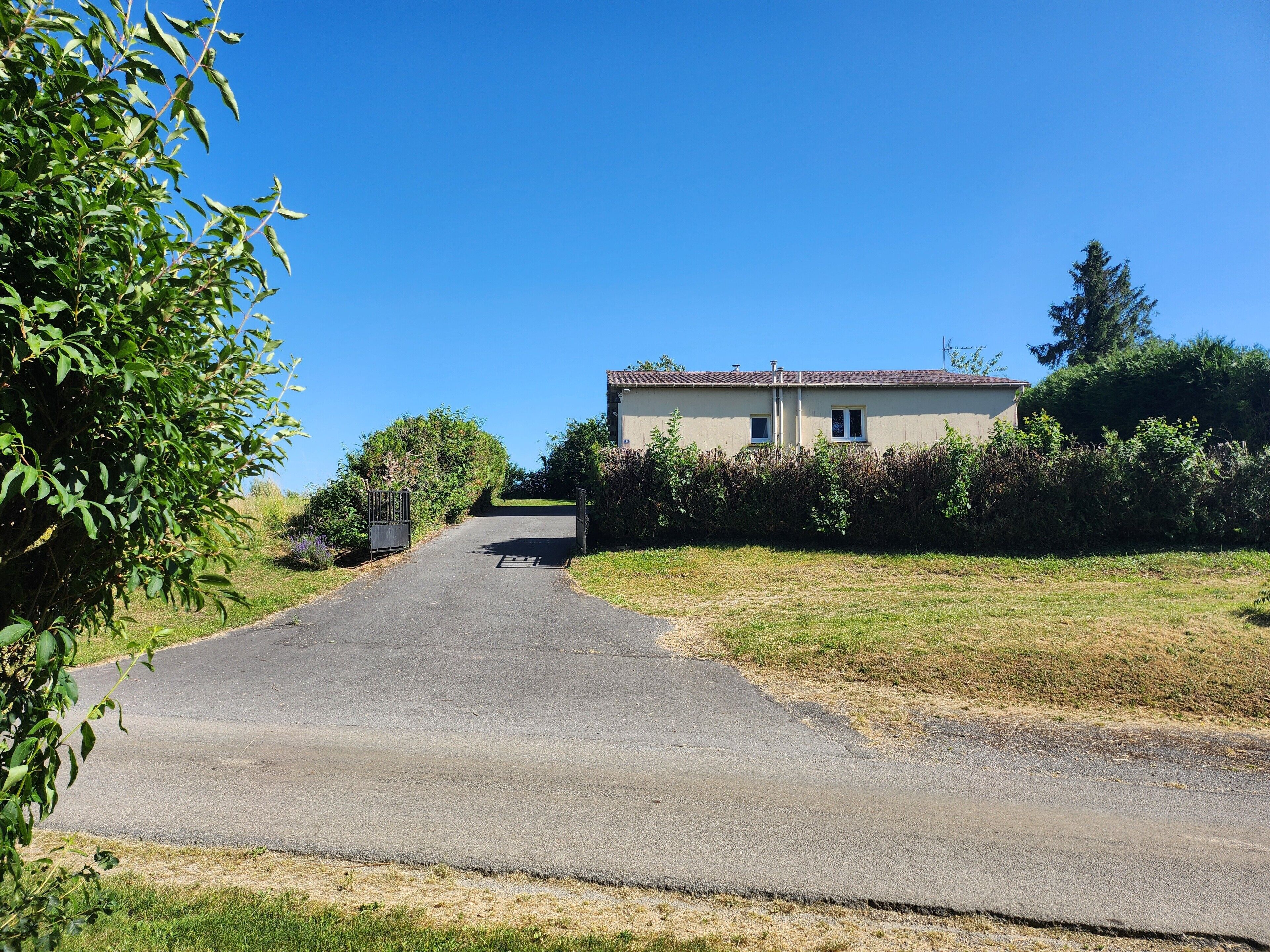 A rural road leading to a two-story house with a tiled roof, surrounded by greenery.