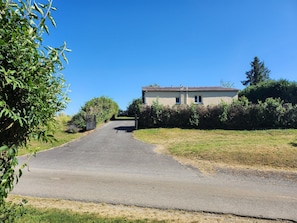 A rural road leading to a two-story house with a tiled roof, surrounded by greenery.