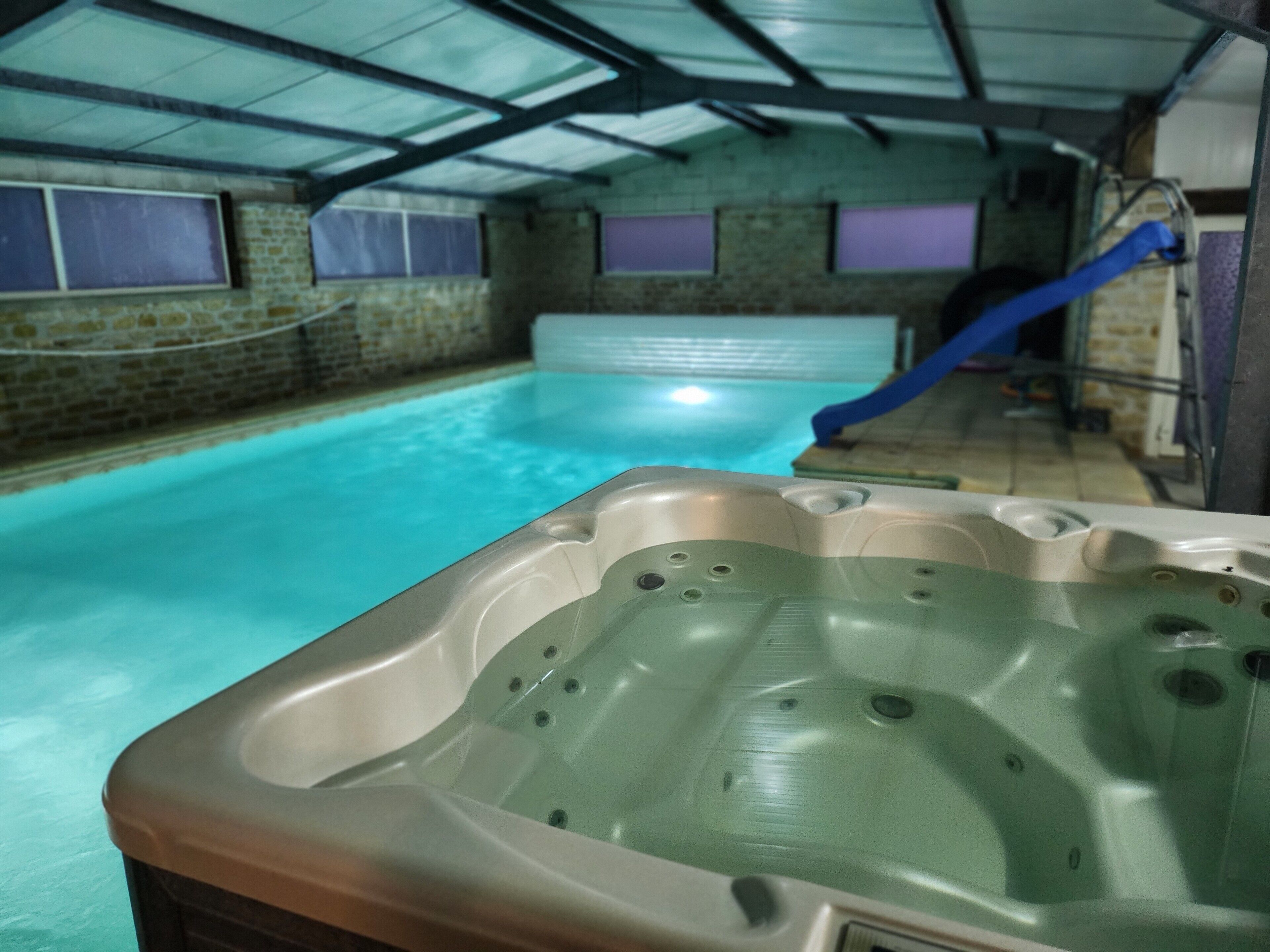 Ein Hallenbad mit einer Whirlpool im Vordergrund und einer Rutsche im Hintergrund.