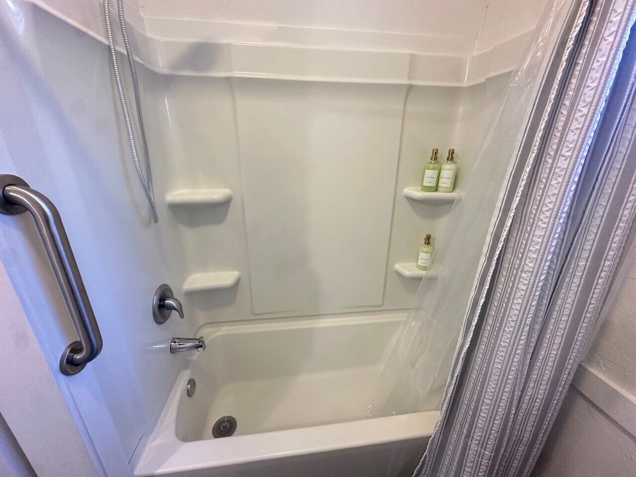 A white bathtub with a shower curtain, a grab bar, and two bottles on a shelf.