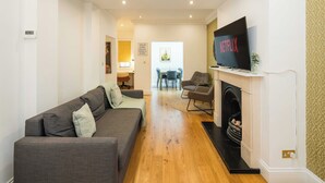 A living room with a sofa, chairs, a fireplace, and a TV mounted on the wall.