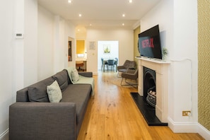 Una sala de estar con sofá, sillas, chimenea y televisión montada en la pared.