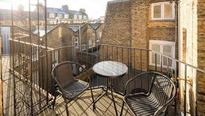 A balcony with two wicker chairs and a small round table, overlooking a brick building with a window.