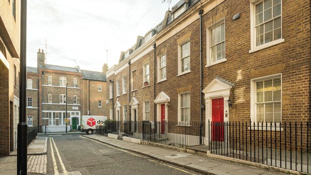 A row of terraced houses with a red door, a white van, and a black fence.