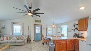 Amplia sala de estar con sofá, mesa de comedor y cocina con armarios de madera y refrigerador blanco.