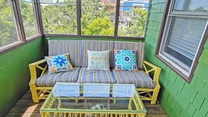 Une véranda aux murs peints en vert, avec un canapé à rayures, deux coussins et une table basse dont le plateau est en verre.