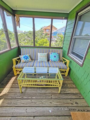 A green-walled porch with a striped sofa, two cushions, and a glass-top coffee table.