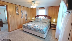 Une chambre à coucher avec un lit, des murs en bois, un ventilateur de plafond et une fenêtre avec des rideaux.