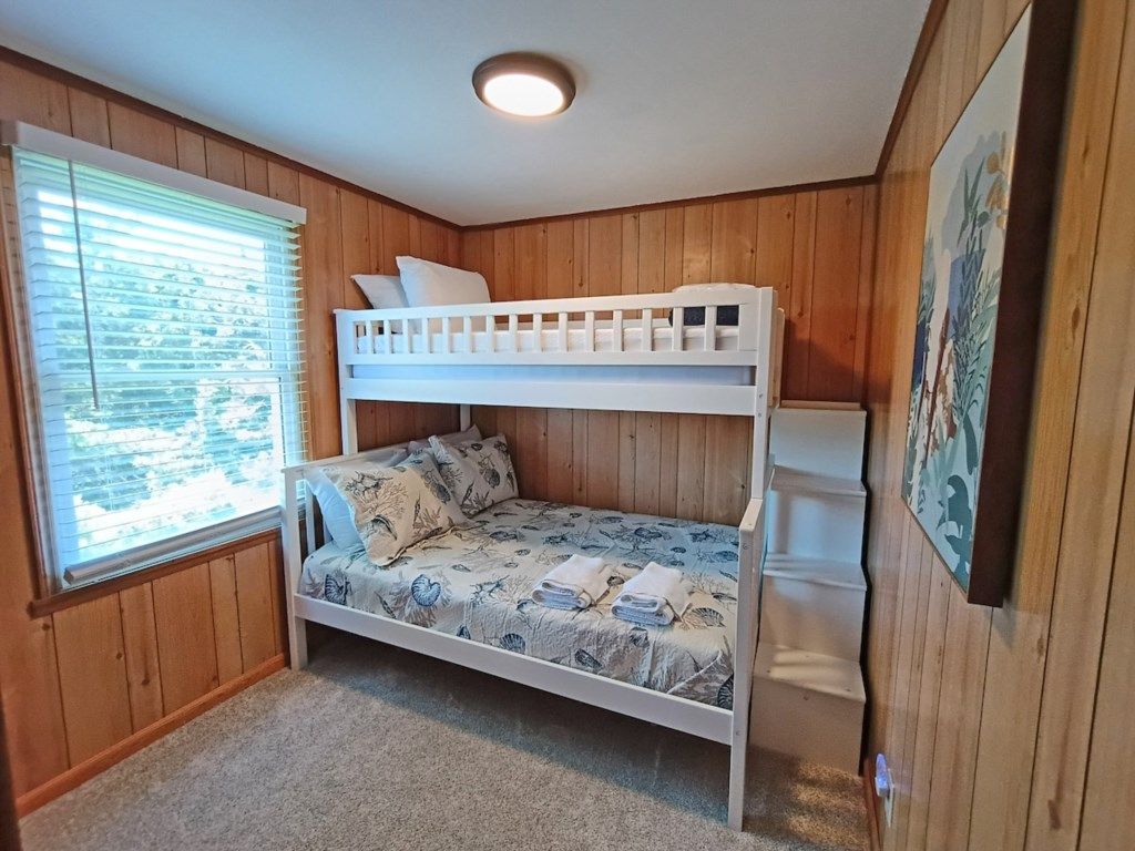 Une chambre avec un lit superposé, une fenêtre, des murs en bois et un luminaire au plafond.