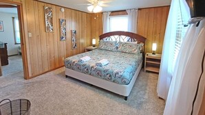 A bedroom with a bed, wooden walls, a ceiling fan, and a window with curtains. - Beach cottage/4min to beach/pets ok/wifi (Salvo)