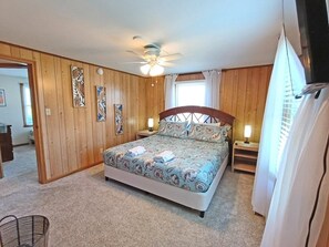 Ein Schlafzimmer mit einem Bett, Holzwänden, einem Deckenventilator und einem Fenster mit Vorhängen.