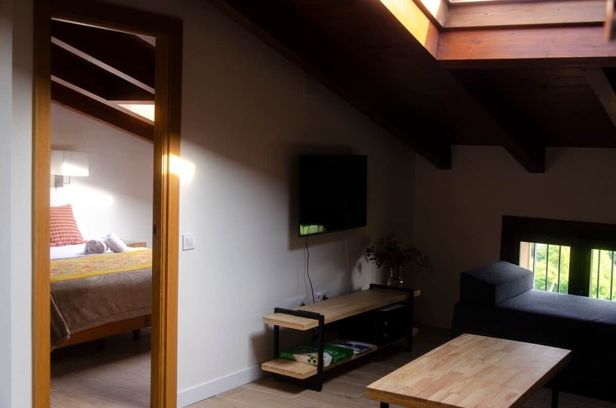 Une chambre avec un lit, un téléviseur fixé au mur, un canapé et une fenêtre donnant sur un beau paysage.