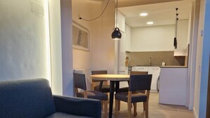 A modern living room with a sofa, a dining table with chairs, and a kitchen area in the background.