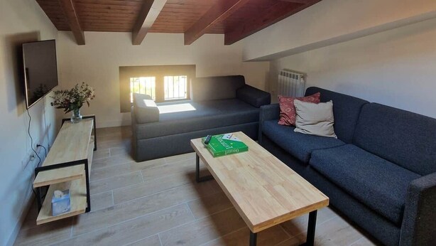 A loft-style room with a sloped ceiling, a wooden floor, a sofa, a coffee table, and a TV mounted on the wall.