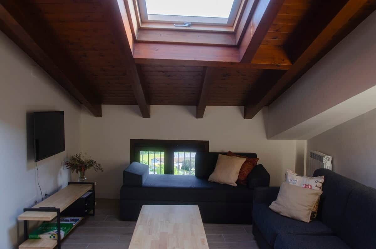 Un salon avec une lucarne, un canapé, une table basse et un téléviseur fixé au mur.