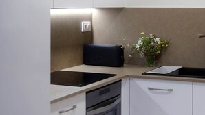 A kitchen with white cabinets, a black oven, a built-in dishwasher, and a small sink with a flower vase.