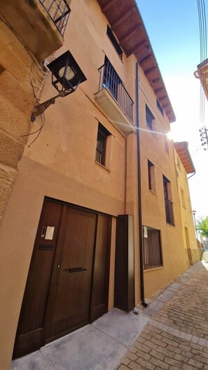 A building with a brown door, a small balcony, and a brick pathway.