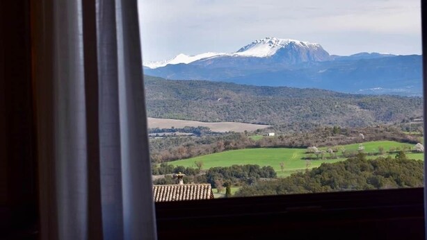 A view of a mountainous landscape through a window with curtains.