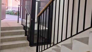 A staircase with a wooden handrail and black balusters, leading to an interior space with a door labeled 'SALIDA' and a tiled floor.