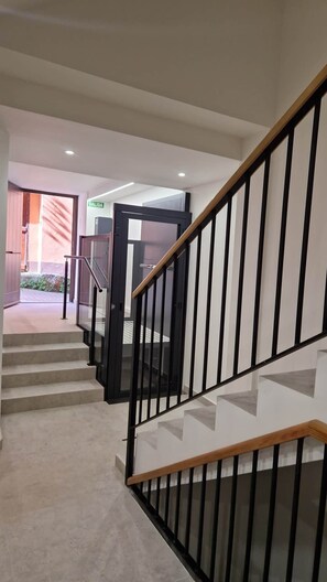 A staircase with a wooden handrail and black balusters, leading to an interior space with a door labeled 'SALIDA' and a tiled floor.