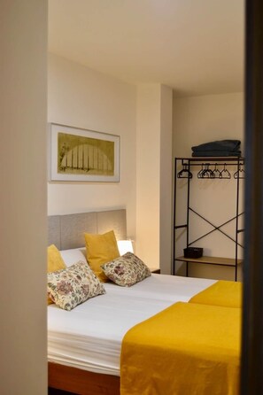 A bedroom with a bed, pillows, a headboard, a wall-mounted artwork, and a metal rack with folded clothes.
