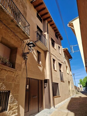 A narrow street with buildings featuring balconies, a street lamp, and a clear blue sky.