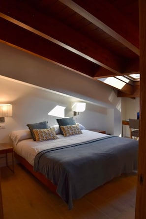 A bedroom with a bed, pillows, a nightstand, a lamp, and a skylight.