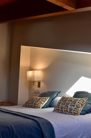 A bedroom with a bed, pillows, a wall-mounted lamp, and a window.