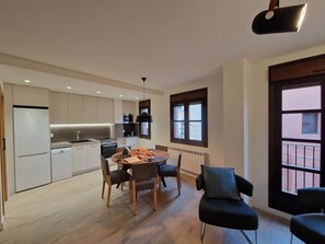 A modern kitchen with white cabinets, a dining table with chairs, and a black pendant light.
