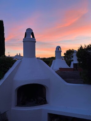 Eine Reihe weißer, moderner Gebäude mit flachen Dächern und Schornsteinen vor einem Abendhimmel.