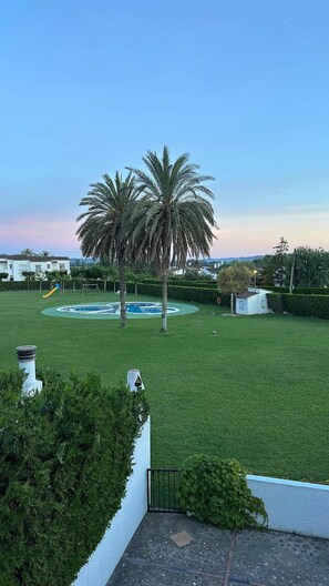 Ein gepflegter Rasen mit einer Palme, einem runden Pool und einem Spielplatz.