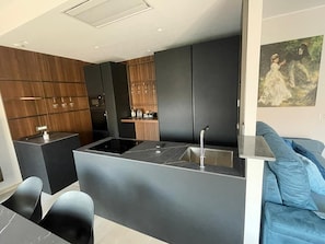 Eine moderne Küche mit dunklen Schränken, einer zentralen Kochinsel mit Spüle und einer Sitzecke mit blauem Sofa.