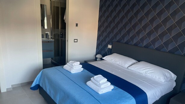 Et moderne hotelværelse med en stor seng, et blåt sengetæppe, hvide puder og en pænt redt seng.