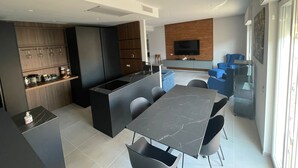 Et moderne køkken med en central ø, indbyggede hårde hvidevarer og et spiseområde med et marmorbord og stole.