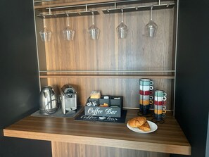 Ein Café-Aufbau mit einer Kaffeemaschine, einem Schild mit der Aufschrift 'Coffee Bar' und einem Teller mit Croissants.