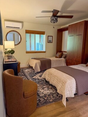 A bedroom with two beds, a ceiling fan, an air conditioning unit, a mirror, a window, and a rug.