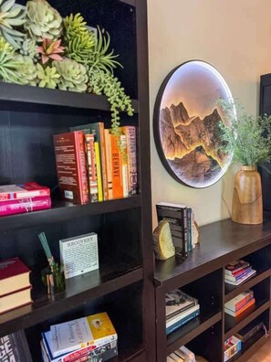 A bookshelf with books, a framed picture of a mountain landscape, and a potted plant.