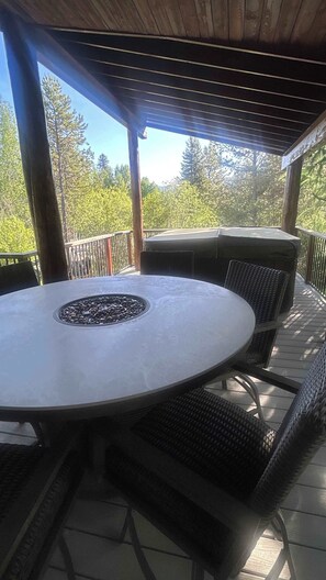 A covered patio with a round table and chairs, a fire pit, and a view of trees.